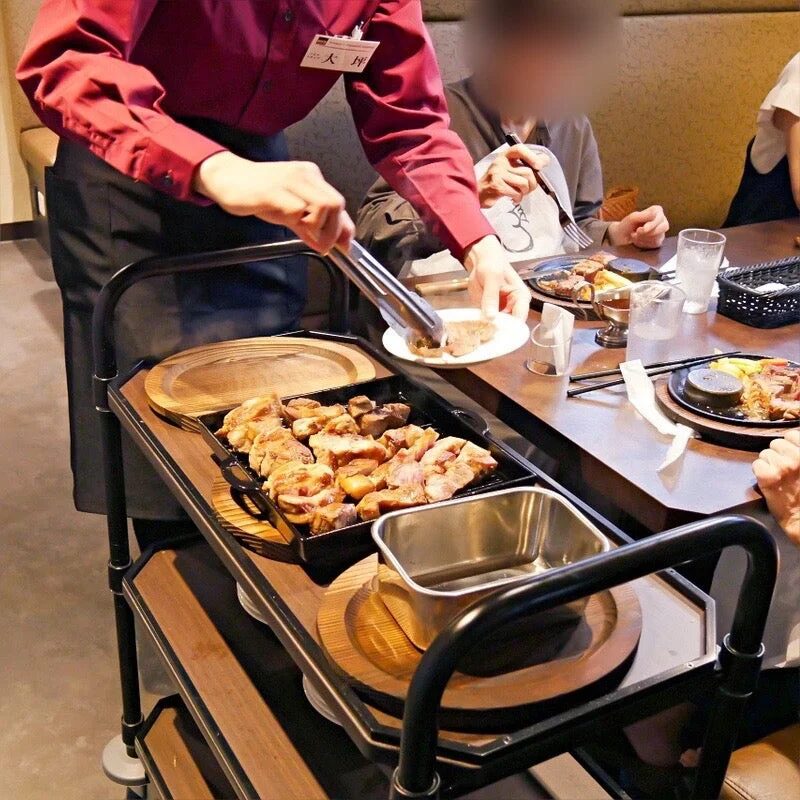 レストランで店員がワゴンに乗せられた熱々の肉料理を客の皿に取り分けている様子
