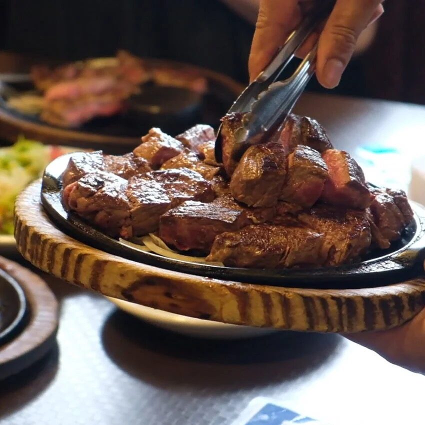 熱々の鉄板に乗せられたサイコロステーキをトングで取り分けている様子